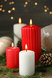 Photo of Burning candles and festive decor on wooden table against blurred Christmas lights