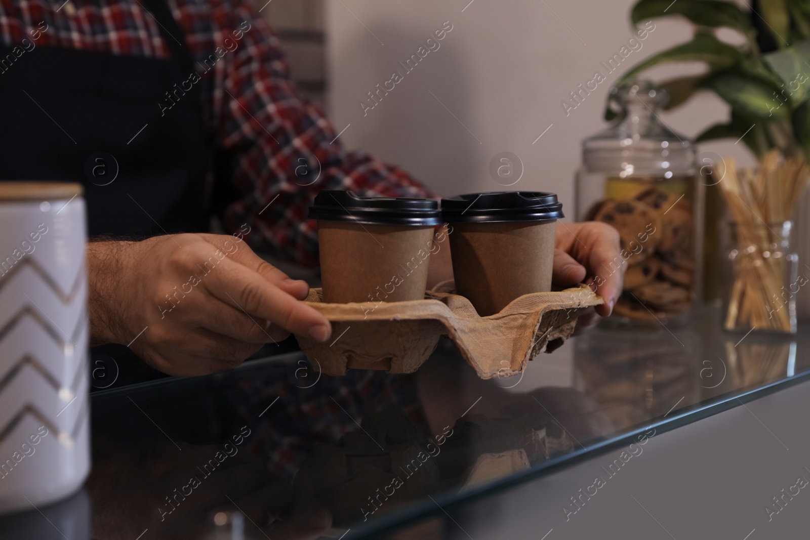 Photo of Barista putting takeaway coffee cups with cardboard holder on glass table in cafe, closeup