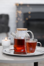 Photo of Teapot, cup of aromatic tea and burning candle on white table indoors, space for text