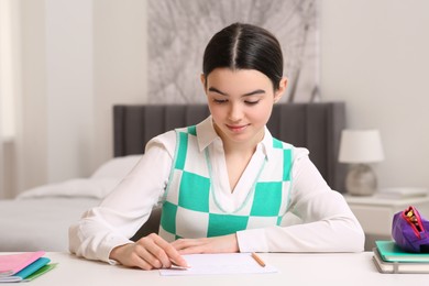 Teenage girl erasing mistake in her notebook at white desk indoors