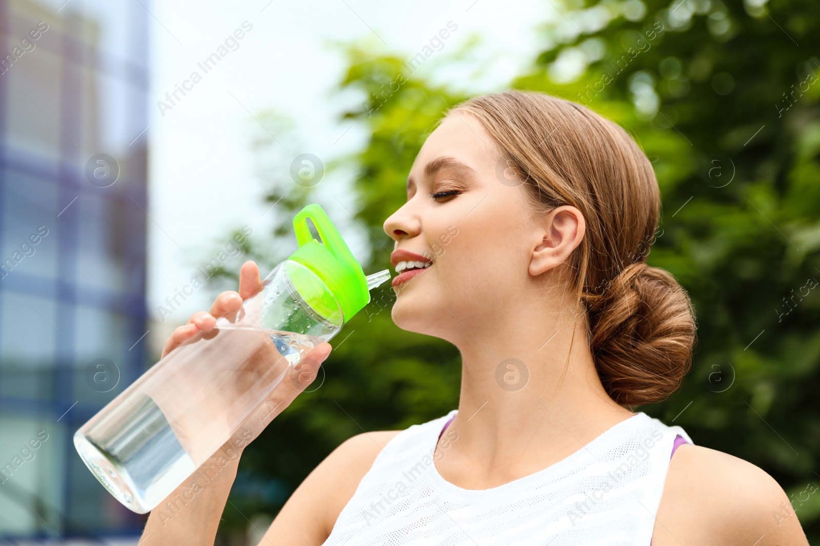 Photo of Young woman drinking water outdoors. Refreshing drink