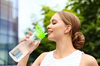 Young woman drinking water outdoors. Refreshing drink