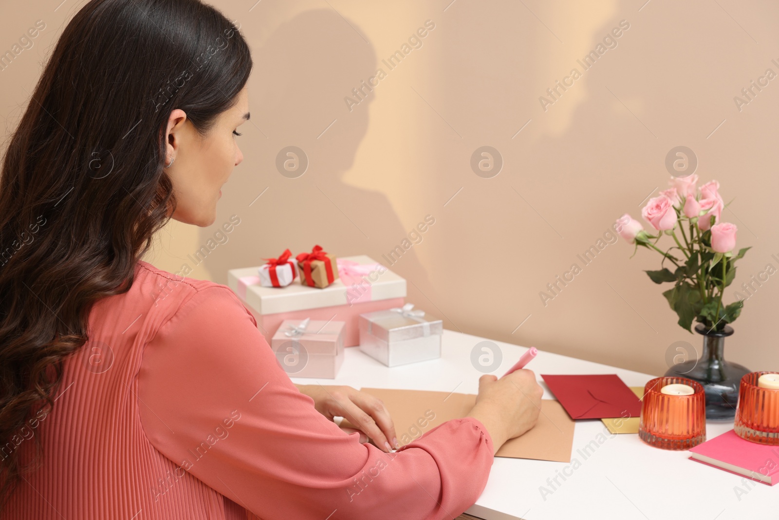 Photo of Young woman writing message in greeting card at table indoors