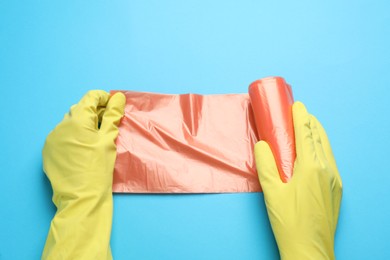 Photo of Janitor in rubber gloves holding roll of orange garbage bags over turquoise background, top view