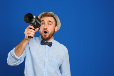 Young man with vintage video camera on blue background. Space for text
