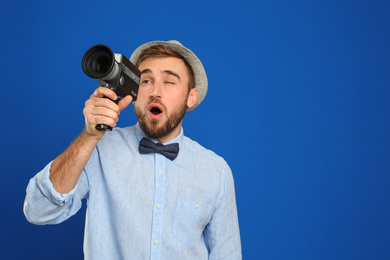 Photo of Young man with vintage video camera on blue background. Space for text