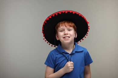 Cute boy in Mexican sombrero hat on grey background, space for text