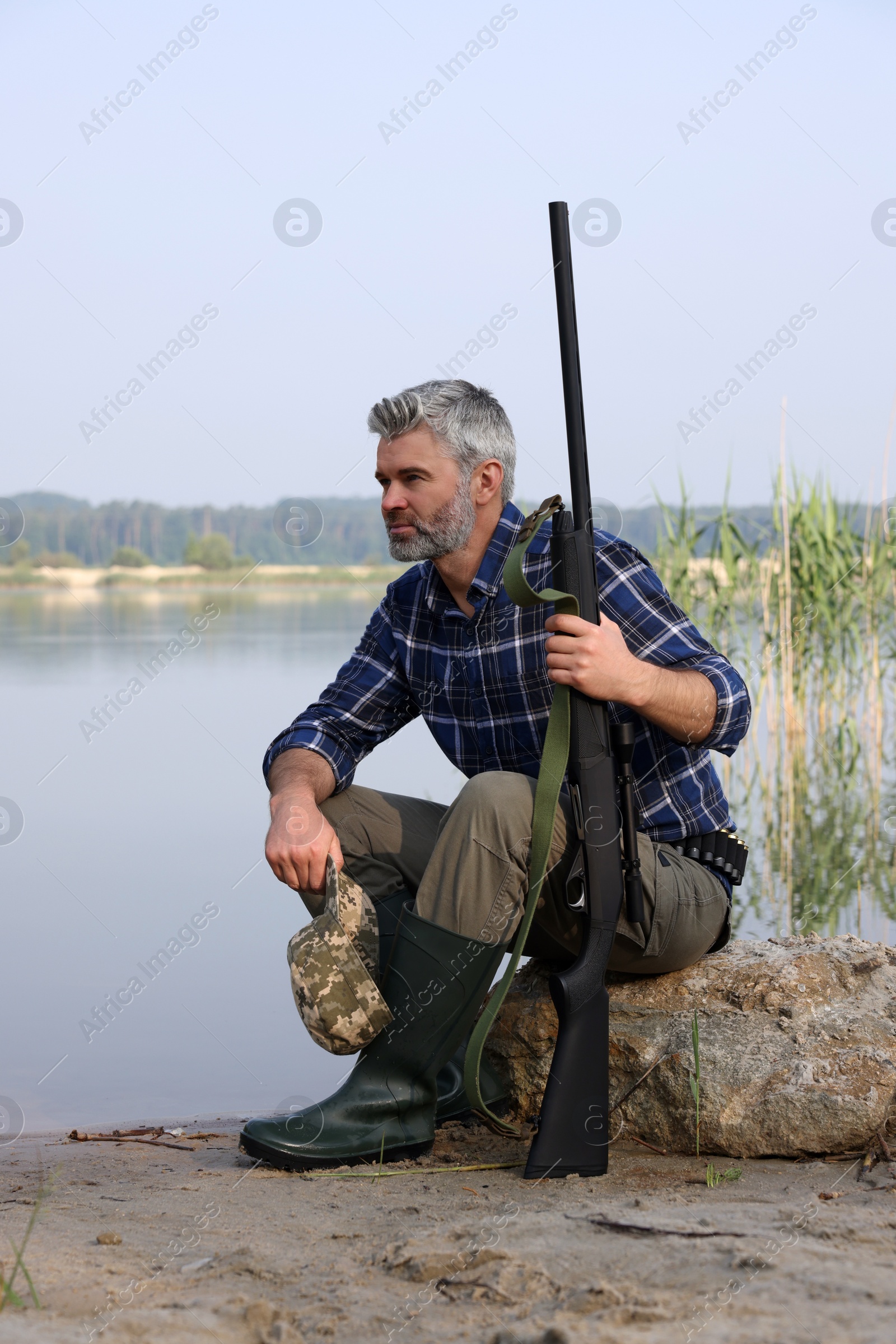 Photo of Man with hunting rifle near lake outdoors