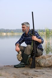 Man with hunting rifle near lake outdoors