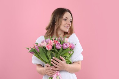 Happy young woman with bouquet of beautiful tulips on pink background