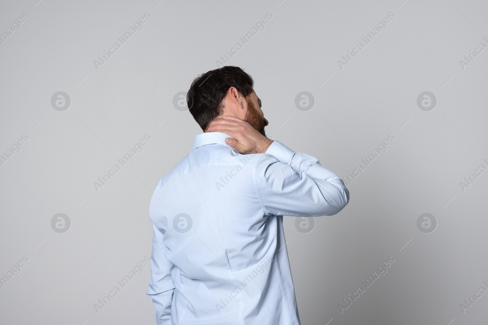 Photo of Man suffering from pain in his neck on light background, back view. Arthritis symptoms