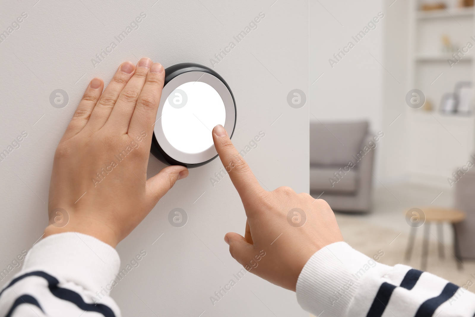 Photo of Woman adjusting thermostat on white wall indoors, closeup. Smart home system