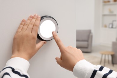 Photo of Woman adjusting thermostat on white wall indoors, closeup. Smart home system