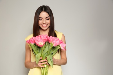 Portrait of beautiful smiling girl with spring tulips on light background, space for text. International Women's Day