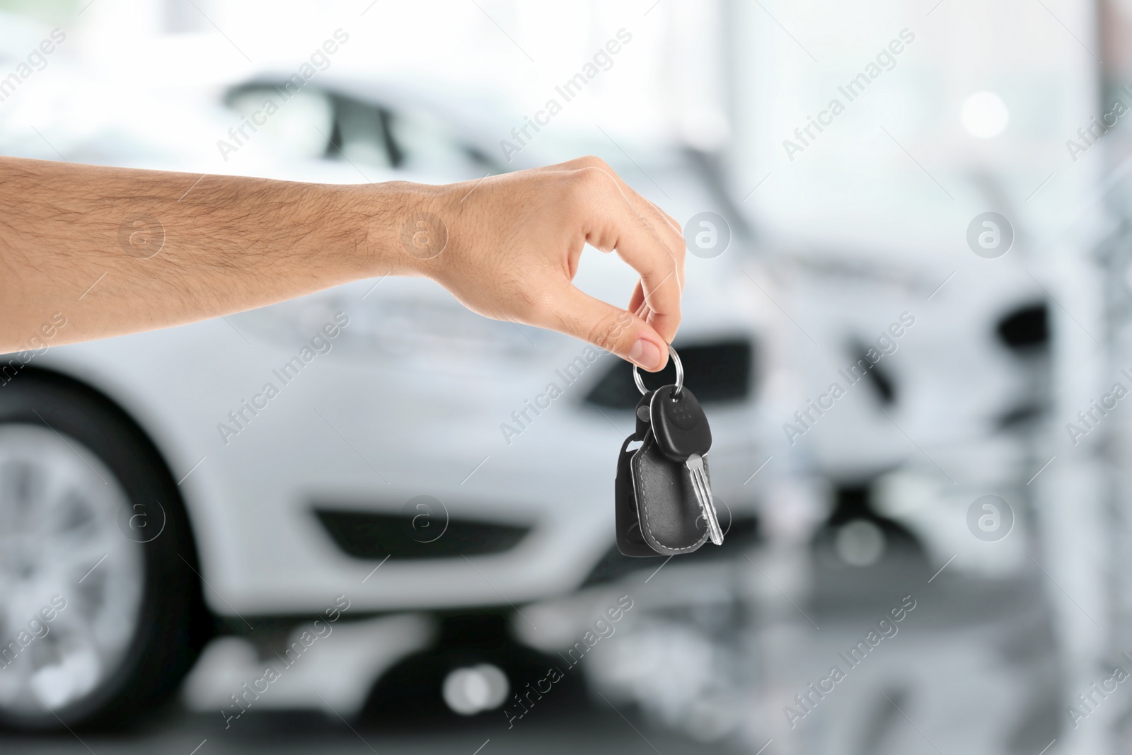 Image of Car buying. Man holding key against blurred automobiles, closeup