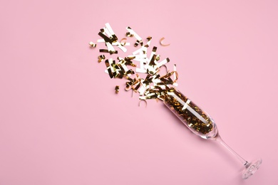 Glass and shiny confetti on pink background, flat lay. Space for text