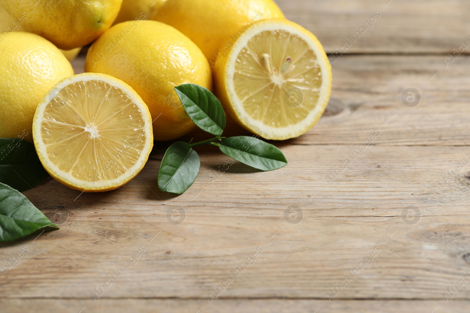 Photo of Fresh lemons and green leaves on wooden table, closeup. Space for text