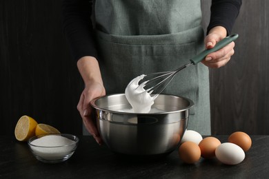 Photo of Woman making whipped cream with whisk at black table, closeup