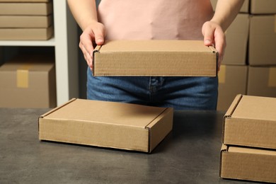 Photo of Packaging goods. Woman with cardboard boxes at grey table indoors, closeup