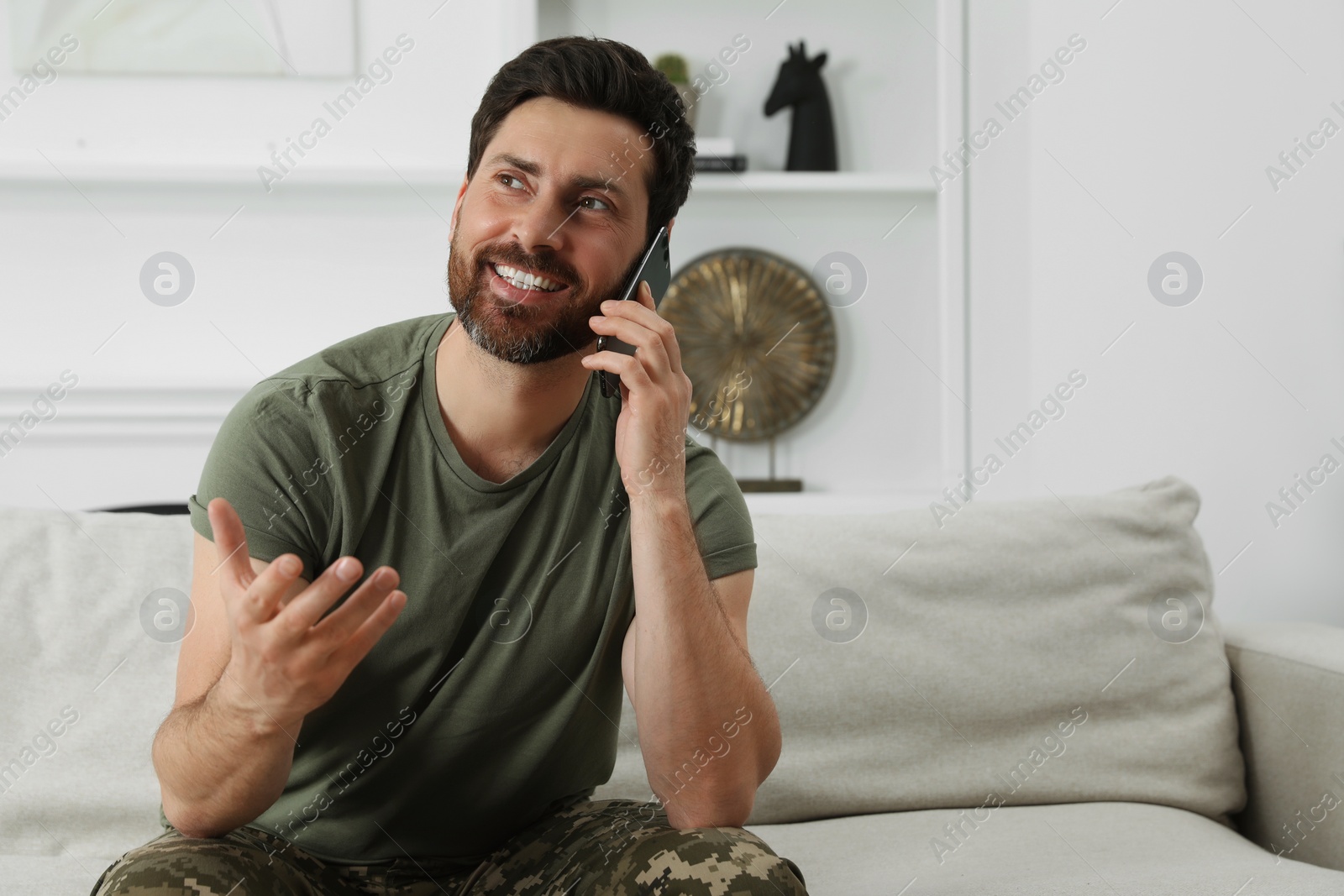 Photo of Happy soldier talking on phone in living room. Military service