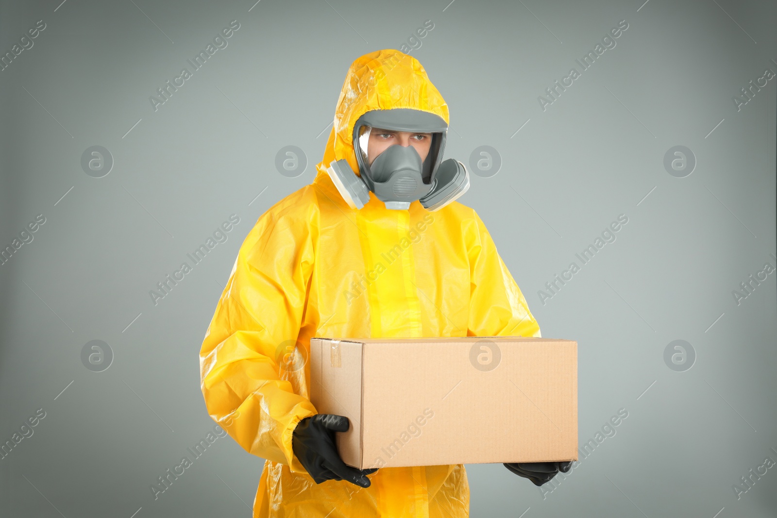 Photo of Man wearing chemical protective suit with cardboard box on light grey background. Prevention of virus spread