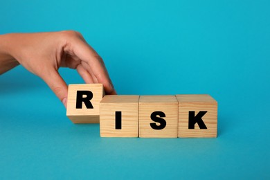 Photo of Woman making word Risk with wooden cubes on turquoise background, closeup