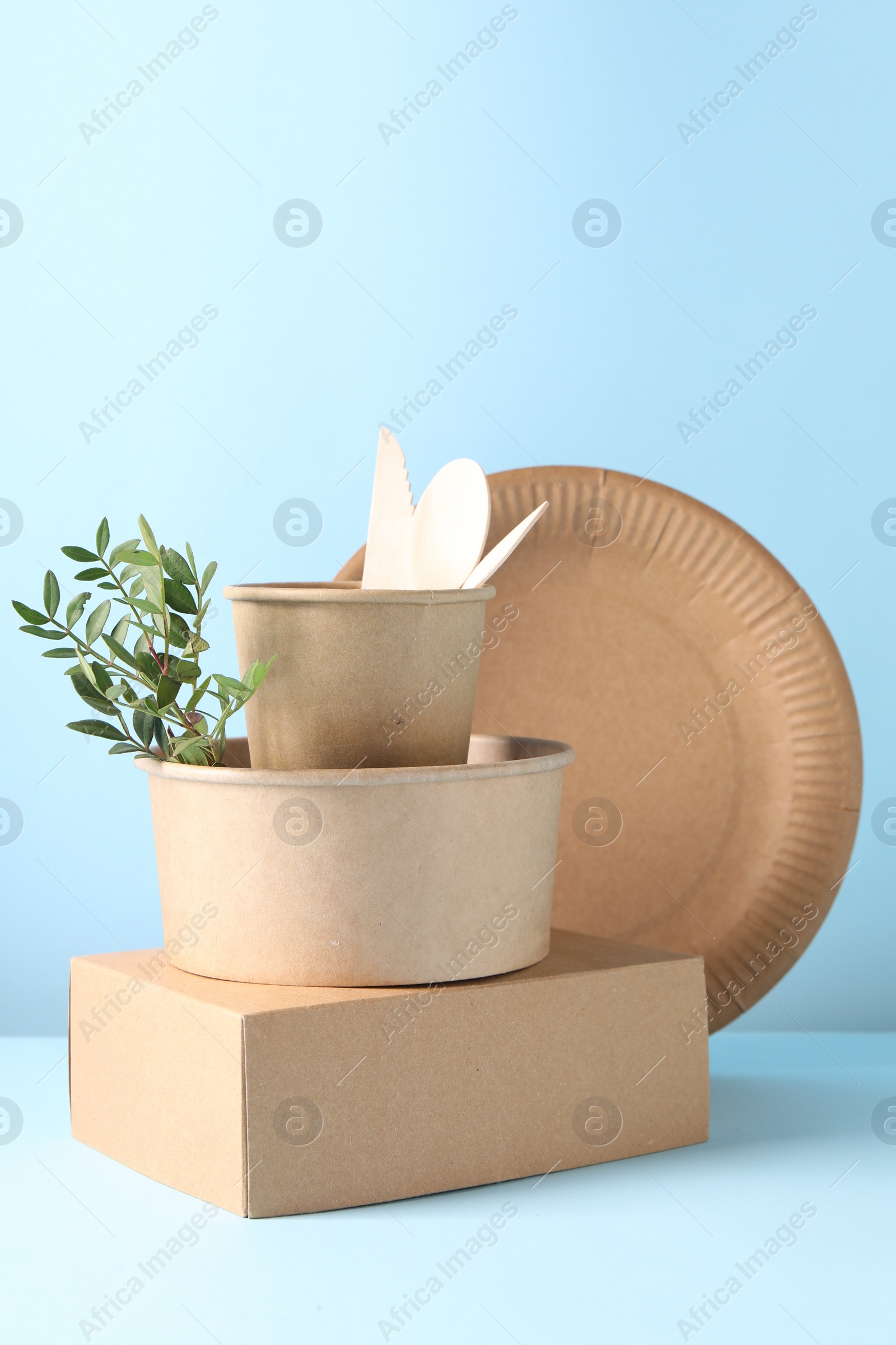 Photo of Eco friendly food packaging. Paper containers, tableware and green twig on white table against light blue background