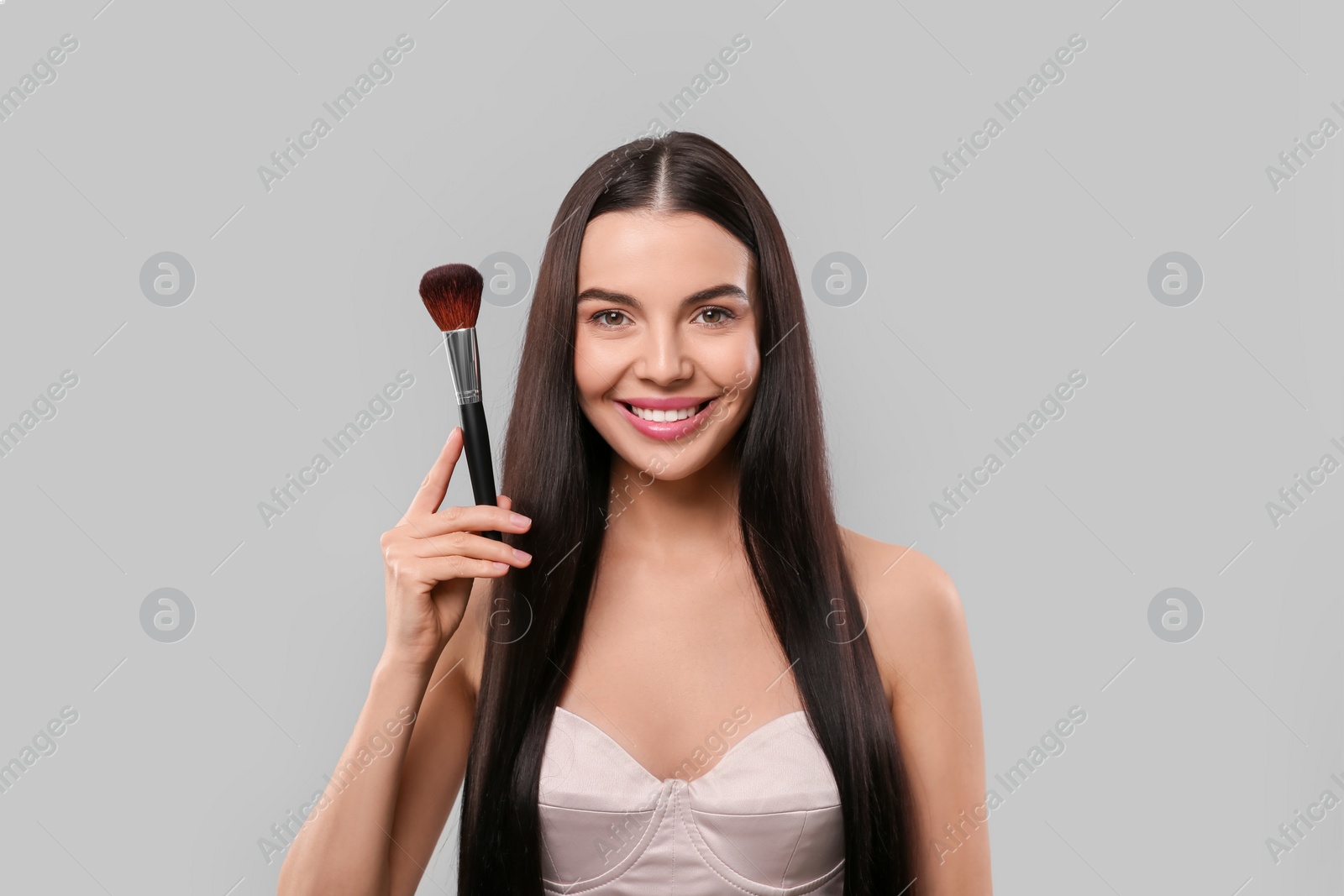 Photo of Happy woman with makeup brush on light grey background