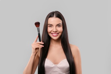 Photo of Happy woman with makeup brush on light grey background