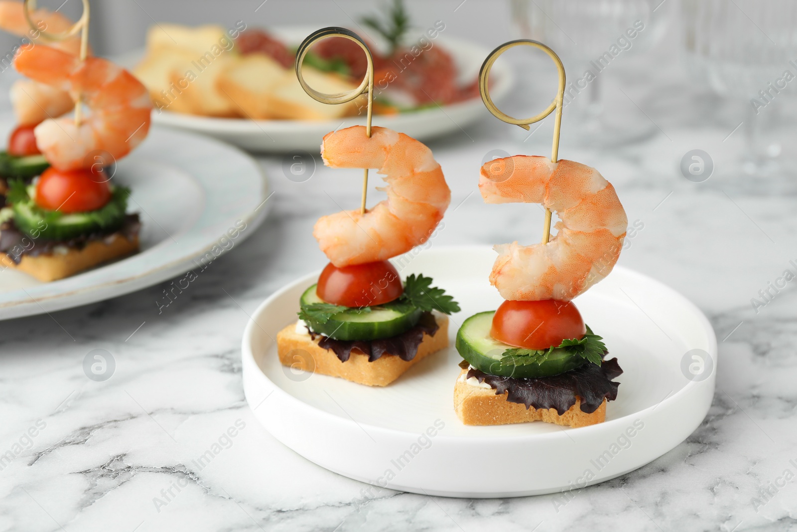 Photo of Tasty canapes with shrimps, cucumber, greens and tomatoes on white marble table, closeup