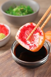 Photo of Holding delicious sushi roll with chopsticks at wooden table, closeup