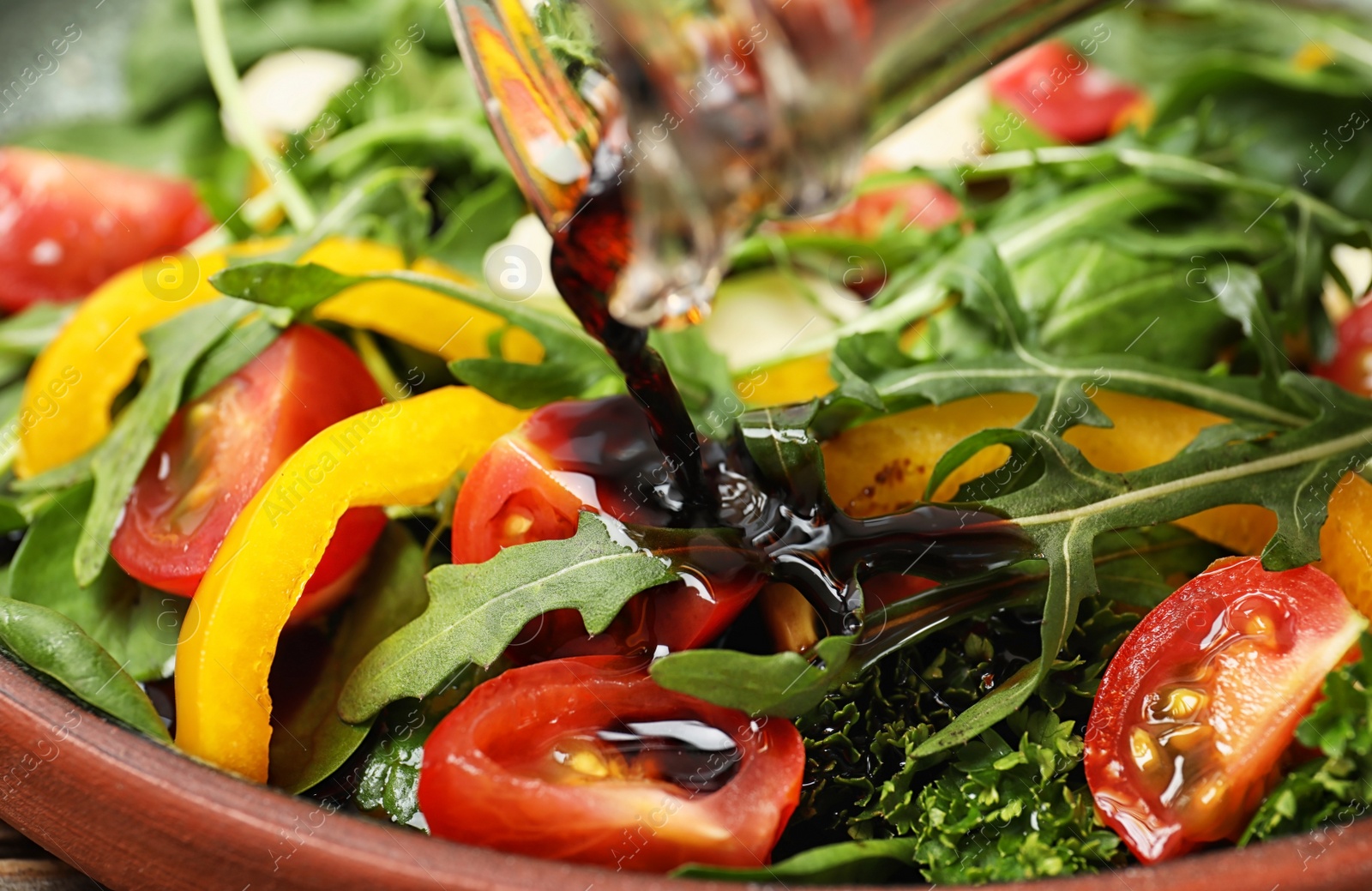 Photo of Pouring balsamic vinegar to fresh vegetable salad on plate, closeup