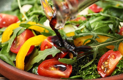 Photo of Pouring balsamic vinegar to fresh vegetable salad on plate, closeup