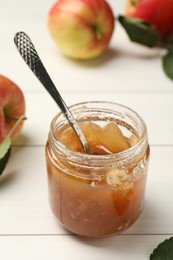 Photo of Tasty apple jam in glass jar and fresh fruit on white wooden table
