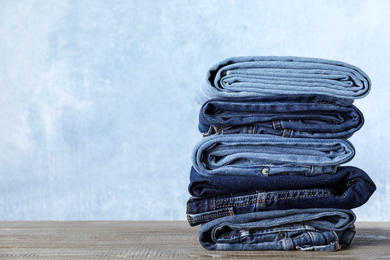 Photo of Stack of different jeans on wooden table against blue background. Space for text