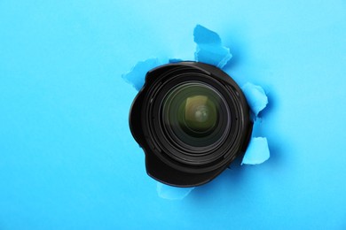 Photo of Hidden camera lens through torn hole in light blue paper