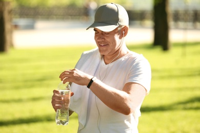 Image of Mature man opening bottlewater after training in park