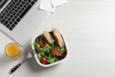 Container of tasty food, laptop, fork and glass of juice on white wooden table, flat lay with space for text. Business lunch