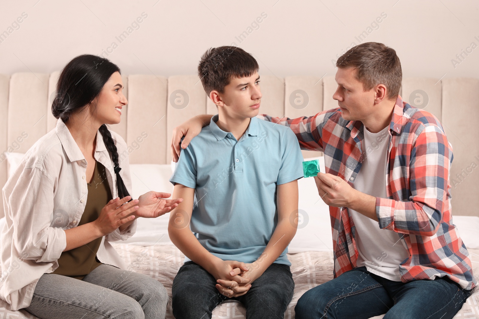 Photo of Parents talking with their teenage son about contraception in bedroom. Sex education concept