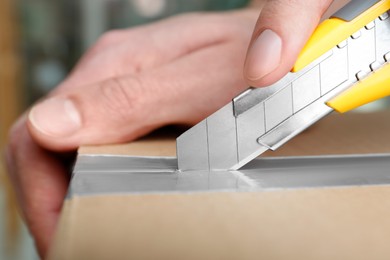 Photo of Man using utility knife to open parcel, closeup