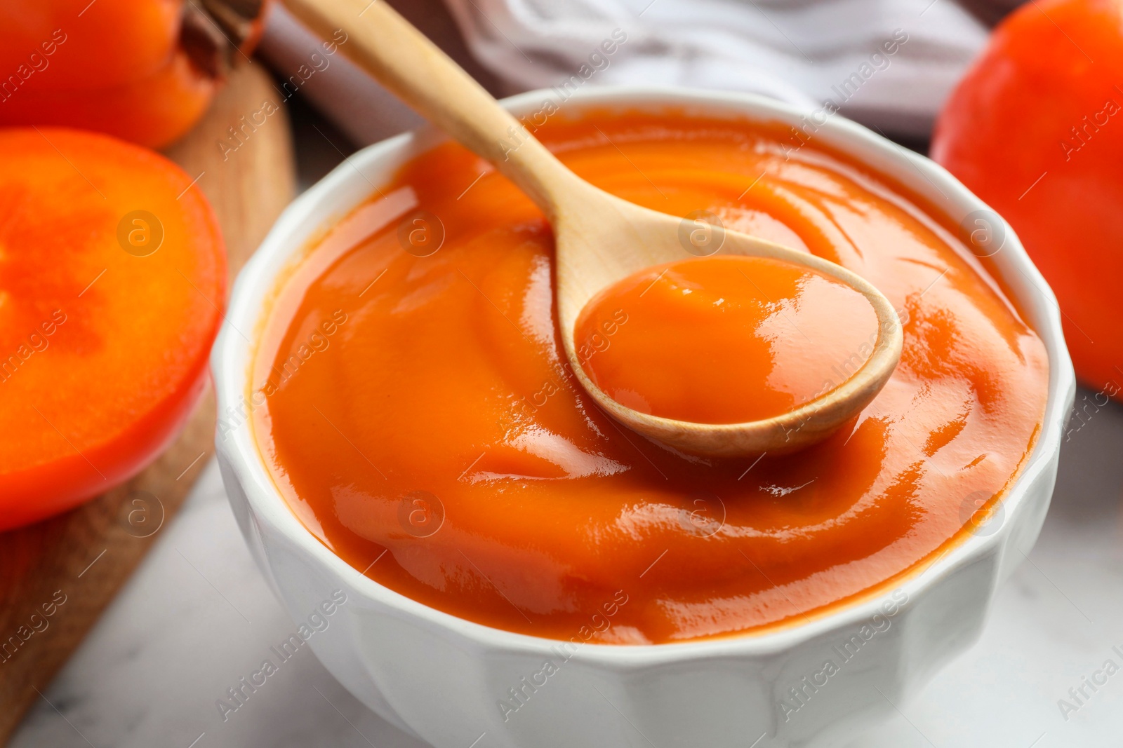 Photo of Delicious persimmon jam and fresh fruits on table, closeup