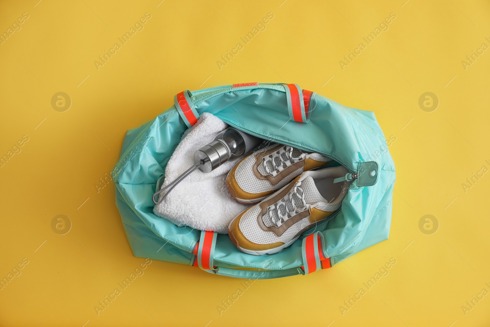 Photo of Gym bag with sports equipment on yellow background, top view