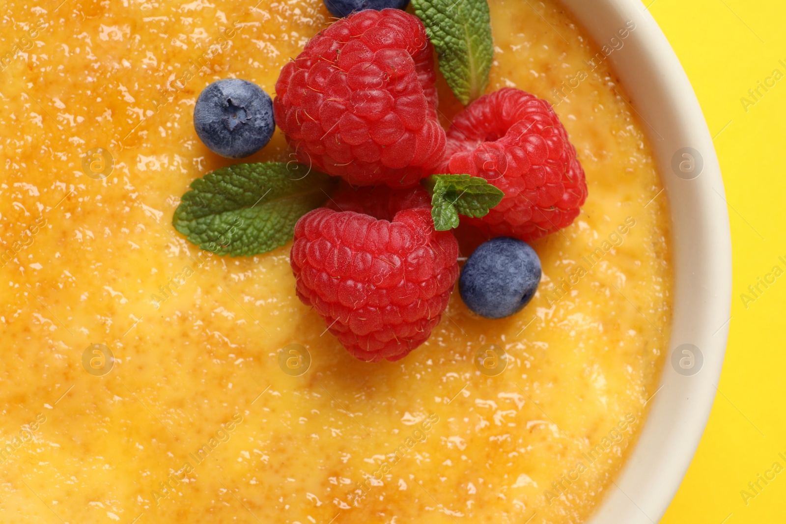 Photo of Delicious creme brulee with fresh berries and mint on yellow background, top view