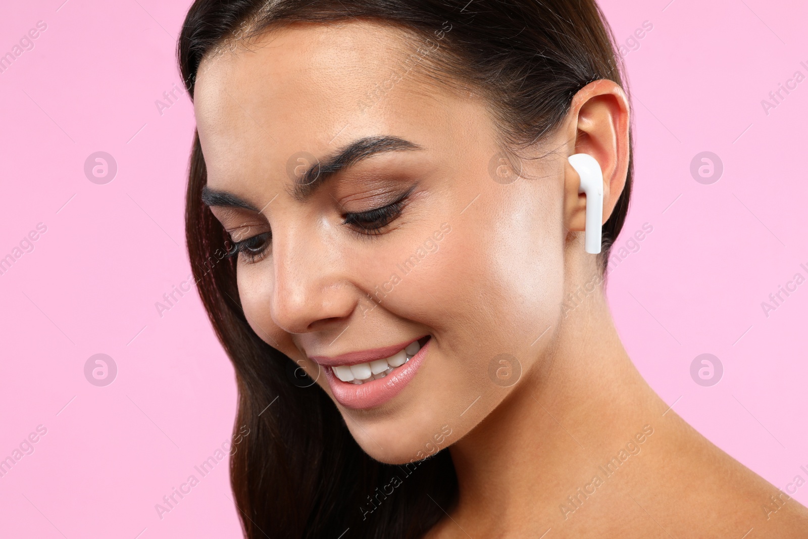 Photo of Happy young woman listening to music through wireless earphones on pink background, closeup