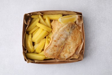 Photo of Delicious fish and chips in paper box on light gray table, top view