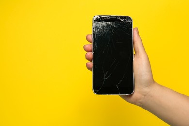 Photo of Woman holding damaged smartphone on yellow background, closeup with space for text. Device repairing