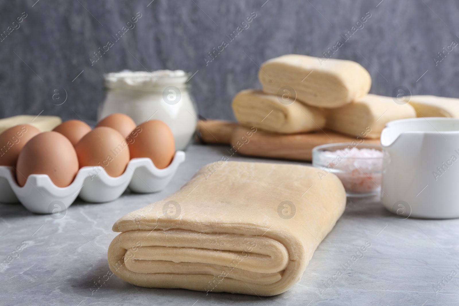 Photo of Raw puff pastry dough and ingredients on grey table