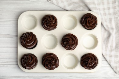 Delicious chocolate cupcakes with cream in baking tray on white wooden table, top view