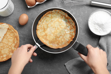Woman holding frying pan with thin pancake at grey table, top view