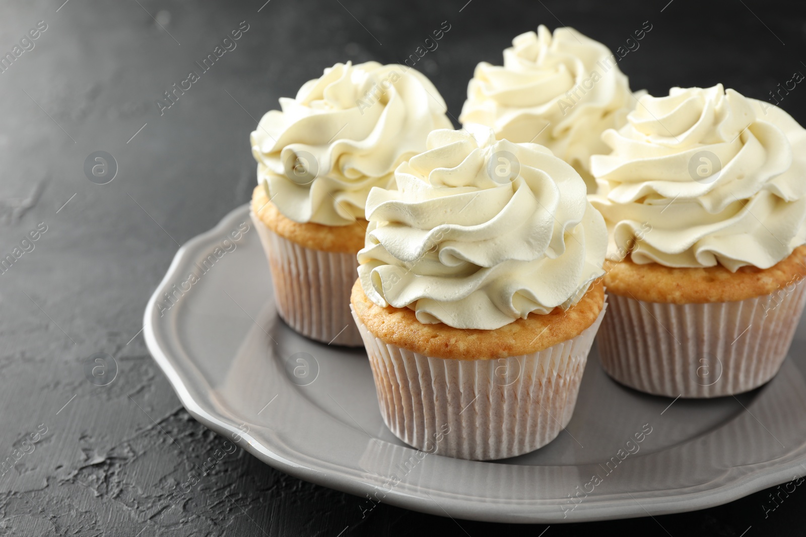 Photo of Tasty cupcakes with vanilla cream on black table, closeup